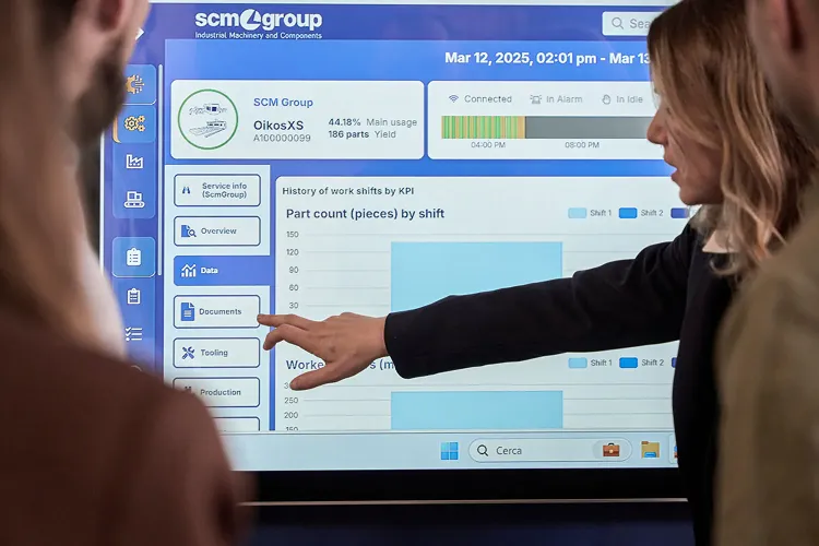 The SCM Digital Portal on a large touchscreen in a plant office — a machine’s part count by shift, with a hand pointing at the chart